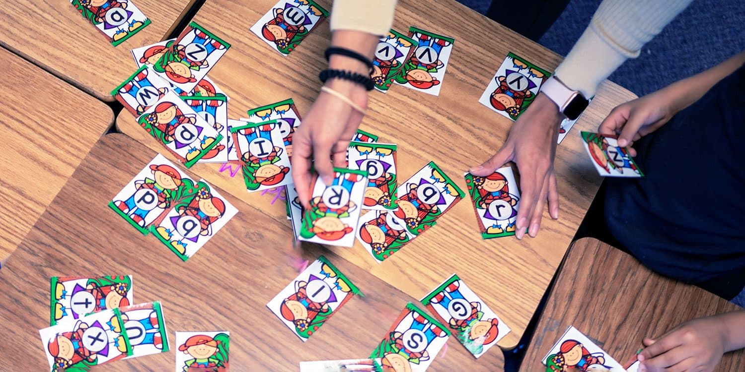 Adult and child hands arranging alphabet cards on a desk.