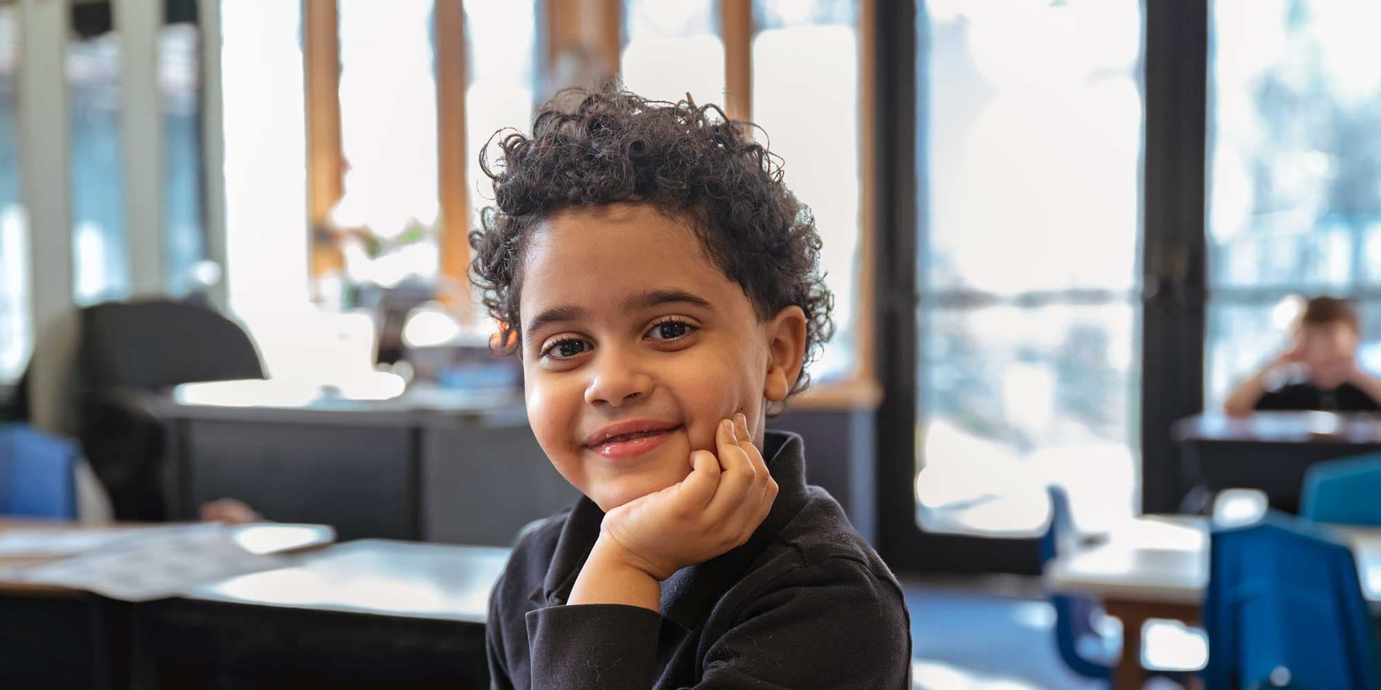 Smiling student with curly hair resting their chin on their hand.